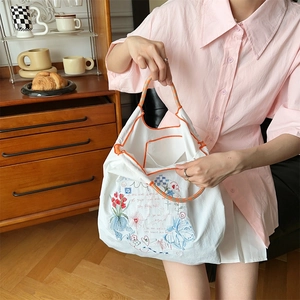 Détail de broderie sur sac cabas en toile blanche avec anses tressées en décor chaleureux