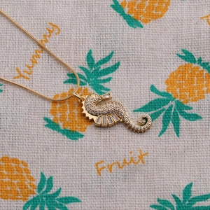 Goldene Seepferdchen-Halskette mit funkelnden Zirkonia auf einem gemusterten Hintergrund