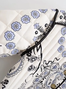 Detail of white quilted fabric with floral print, metal button, and black edge piping