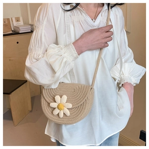 Close-up of beige woven saddle bag with 3D white flower detail and textured strap