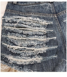 Close-up detail of heavy distressed denim texture and frayed hole design on blue shorts