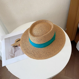 Detailed top view of a flat top straw sun hat with a blue ribbon on a white table