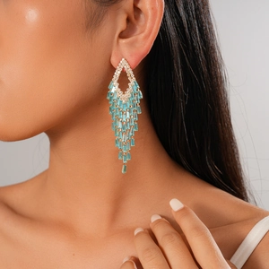 Macro detail of gold-plated tassel earrings featuring light blue rectangular zircon stones