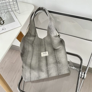 Detail of grey tie-dye canvas tote bag featuring a white woven label on modern chair