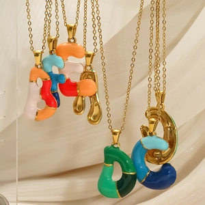 Colliers avec pendentifs lettres en émail coloré et chaînes dorées sur tissu élégant