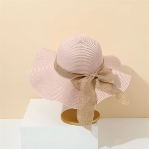 Close-up of pink woven sun hat featuring a brown linen ribbon bow on a golden display stand