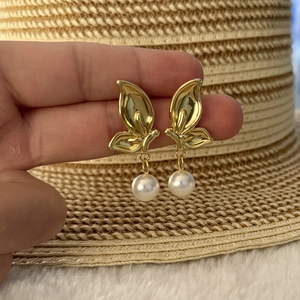 Macro shot of gold butterfly earrings with white pearls and detailed metal texture