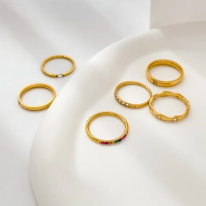 Close-up of set of six gold-plated rings with rainbow stones and zircons on white ceramic