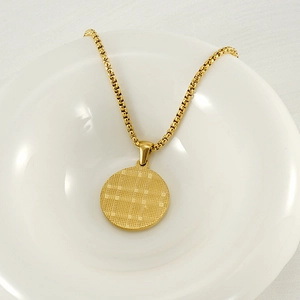 Detailed close-up of 18k gold-plated zodiac pendant with textured grid finish in a white bowl