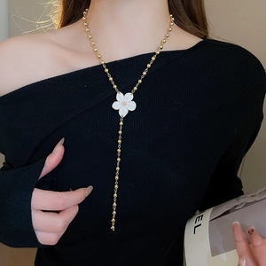 Detail of Y-shaped gold bead necklace with white enamel flower on black garment