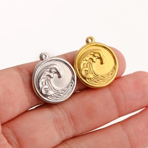 Macro view of gold and silver round ocean wave charms held between fingers