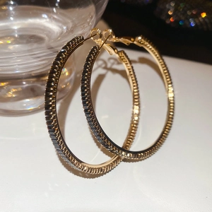 Detailed close-up of gold hoop earrings with black rectangular crystals and textured edges