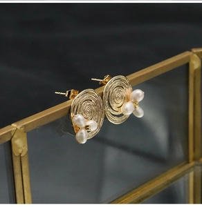 Detail view of gold spiral disk earrings with three natural pearls on a vintage frame