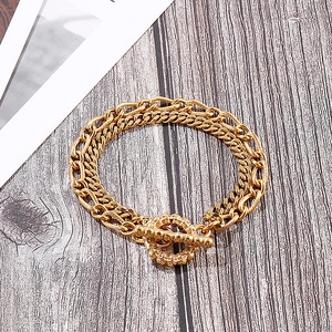 Detail of golden double-layer chain bracelet with textured toggle clasp on wood background
