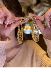 Detail view of golden metal tassel earrings held by hand to show elegant fringe movement