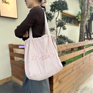 Detail of light pink striped canvas tote bag featuring pink Bonjour embroidery and drawstring