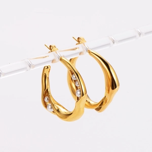 Golden wavy C-shaped hoop earrings with white pearls on a minimalist display stand