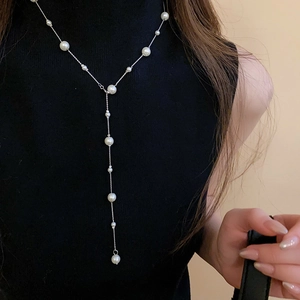 Close-up of elegant Y-shaped pearl necklace on black sweater showing draped jewelry detail