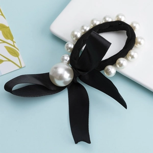 Elegant black elastic hair tie with white pearls and fabric bow accessory on light blue base