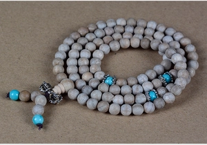 Macro detail of 108 camphor wood beads with turquoise accents and a metal Vajra pendant
