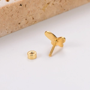 Macro detail of gold butterfly stud earring with screw back on a natural stone surface