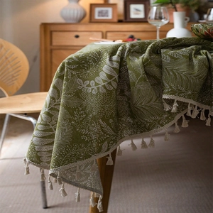 Detail of green linen tablecloth with white leaf patterns and cream tassel trim