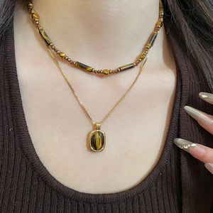 Close-up of layered tiger eye stone necklaces with gold pendant on brown knitwear