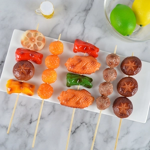 Spiedini di barbecue artificiali realistici con funghi e carne su un piatto bianco