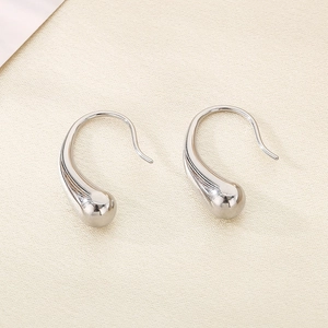 Minimalist silver teardrop hook earrings displayed on elegant off-white silk fabric