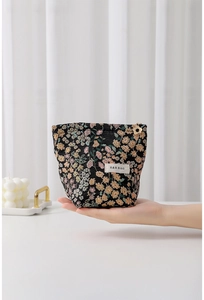 Detailed shot of a floral jacquard makeup bag with a gold petal zipper pull and woven tag