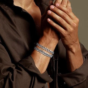 Close-up of two silver stainless steel Cuban links on male wrist with warm lighting