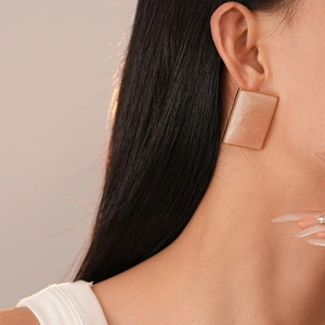 Close-up of elegant gold square earrings with pearlescent resin on a model's ear