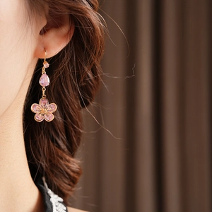 Detailed close-up of gold drop earrings with pink zircon flower charms worn by model
