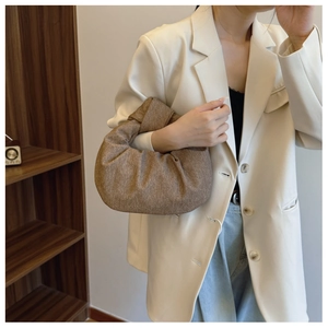 Close-up of brown textured dumpling bag with pleated details held by a model in a suit