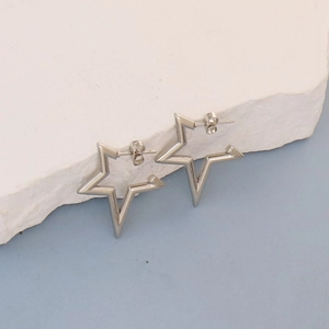 Polished silver star shaped hoop earrings on white stone display with blue background
