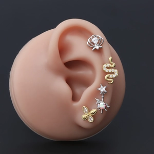 Macro detail of various zircon stud earrings on an ear model showing intricate metal designs