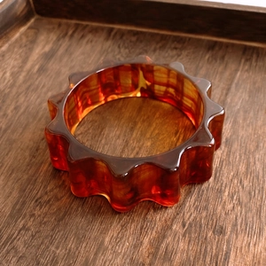 Détail macro du bracelet en résine ambrée au design bord dentelé sur plateau bois