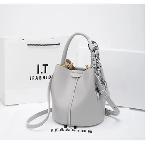 Detail of light gray leather bucket bag with litchi grain and a stylish silk handle scarf