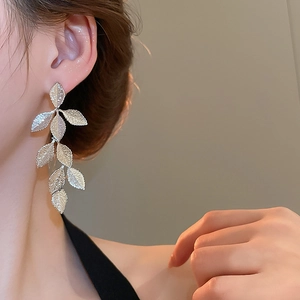 Detail view of long silver leaf tassel earrings with metallic texture on model's ear