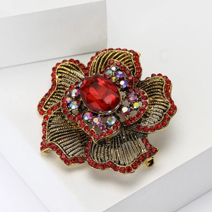 Vintage gold flower brooch with red crystals and rhinestones on a white stand