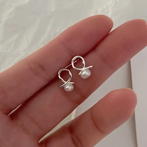Close-up of 925 sterling silver ribbon knot stud earrings with delicate natural pearls