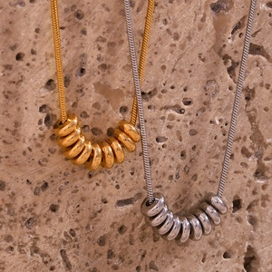 Close-up of gold and silver snake chain necklaces with stacked ring pendants on stone