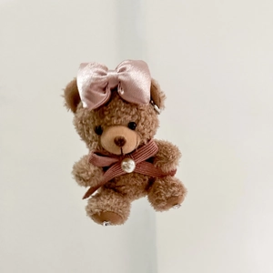 Cute brown plush teddy bear with pink satin bows and pearl detail on white background