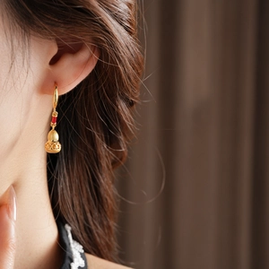 Close-up of gold gourd pendant earrings with brushed texture and red bead detail