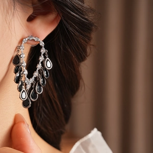 Close-up of model wearing sparkling silver tassel earrings with black teardrop pendants