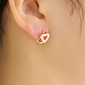Gros plan de boucles d'oreilles cœur dorées avec émail blanc sur l'oreille d'un modèle