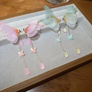 Detailed view of butterfly tassel earrings with gauze wings on a gray velvet tray