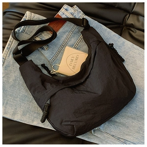 Dettaglio della borsa a tracolla in nylon nero stropicciato su sfondo denim casual