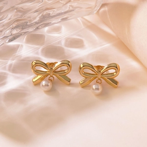Gold bow earrings with white pearls on pink satin background with light reflections