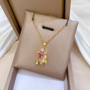 Close-up of gold butterfly necklace with pink gemstone and pearl on white silk fabric